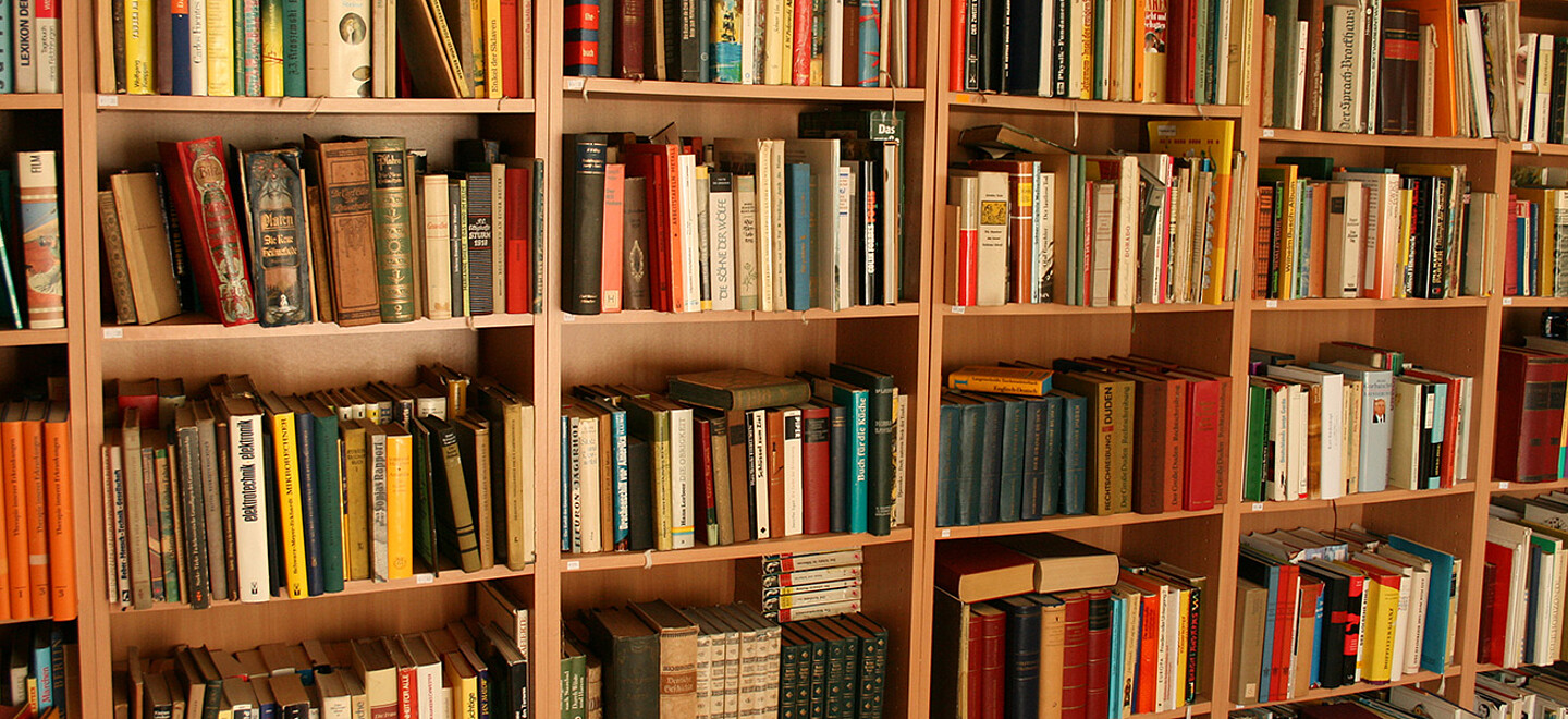 Nahaufnahme eines Bücherregals aus Holz, bis oben hin gefüllt mit Büchern.