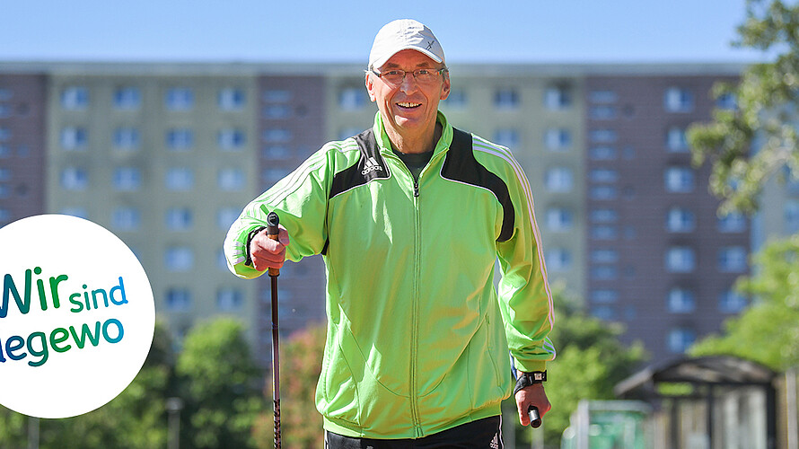 Das Bild zeigt Uwe Tolle beim Nordic Walking auf einen Sportplatz. Er trägt eine grüne Laufjacke und ein Basecap. Im Hintergrund ist verschwommen ein Plattenbau in Marzahn zu erkennen. 