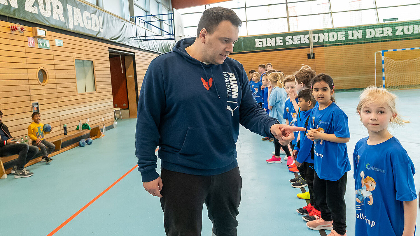 Kinder stehen in einer Turnhalle in einer Reihe. Nick Poethke zählt sie ab bzw. teilt sie in Gruppen ein.