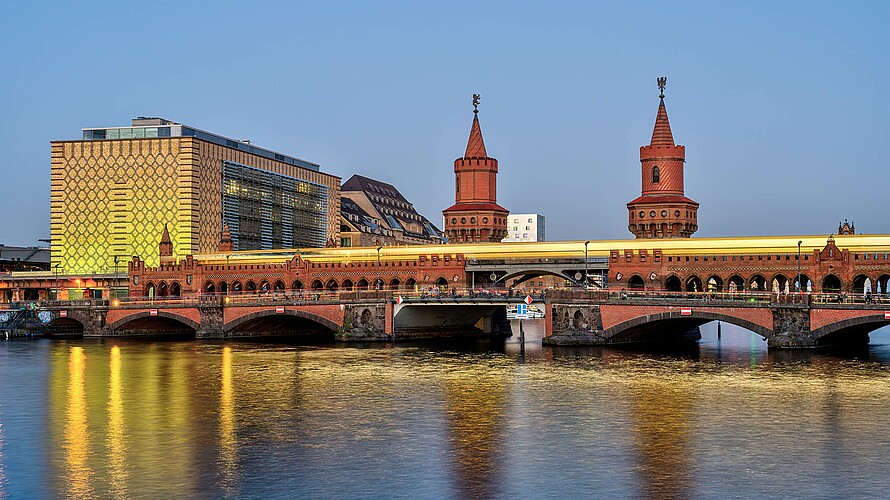 Blick vom Wasser auf eine beleuchtete Brücke aus rotem Stein.