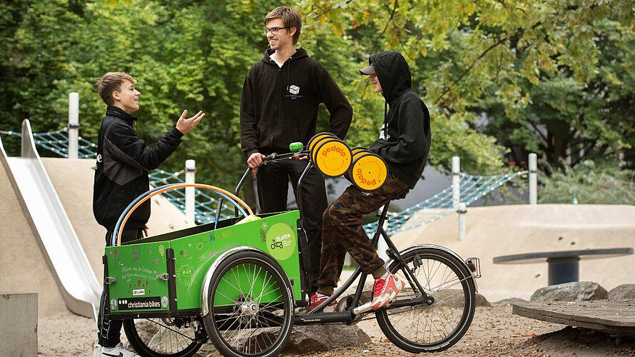 Mann und Jungs unterhalten sich, Junge sitzt auf Lastenrad.