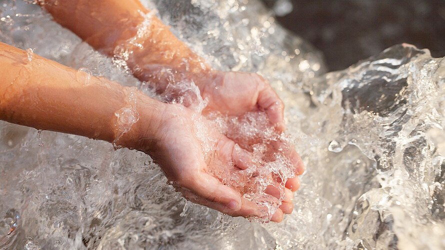 Zwei Kinderhände fangen literweise Wasser auf.