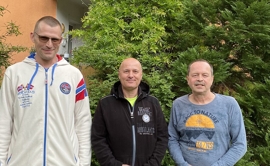 Zu sehen sind Sebastian Runge, Mario Kübler und Bernd Schumann von den Beetbrüdern vor einer grünen Hecke in ihrem Garten in der Pechsteinstraße.