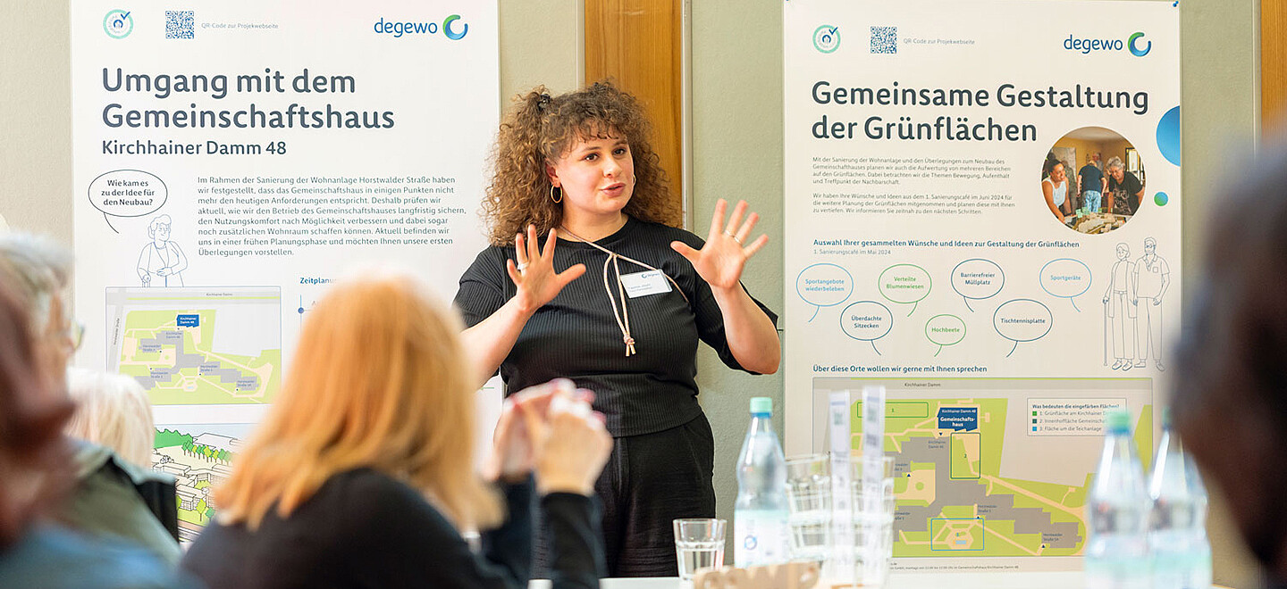 Eine Mitarbeiterin von degewo informiert auf einer Veranstaltung über die geplanten Maßnahmen. Mietende hören zu.