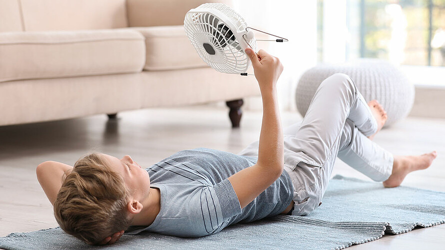 Junge liegt auf dem Boden und richtet einen Ventilator auf sich