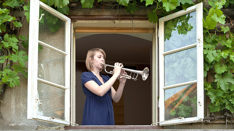 Frau spielt am offenem Fenster Trompete