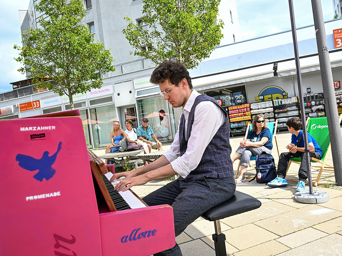 Ein Mann sitzt im Anzug an einem pinken Klavier und spielt Musik auf der Marzahner Promenade.