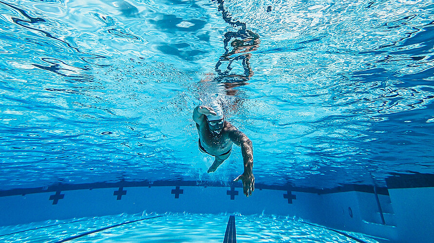 Unterwasseraufnahme eines männlichen Schwimmers in einem großen blauen Schwimmbecken.