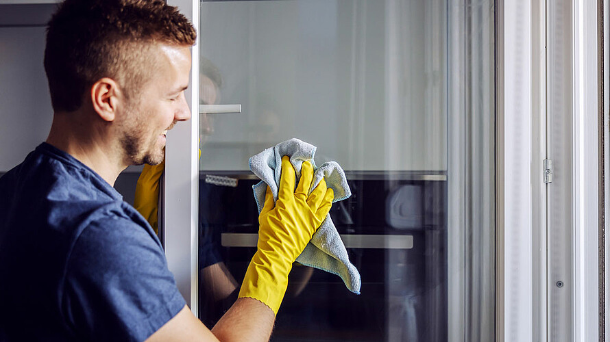 Ein Mann wischt ein Fensterglas mit einem Lappen.