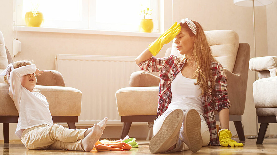 Mutter und Tochter sitzen nach dem Frühjahrsputz erschöpft am Boden.