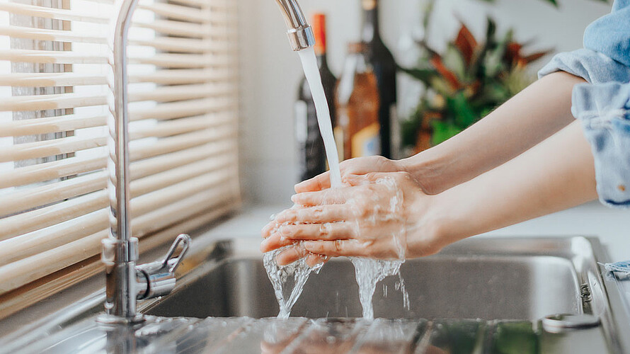 Person wäscht Hände unter laufendem Wasserhahn.