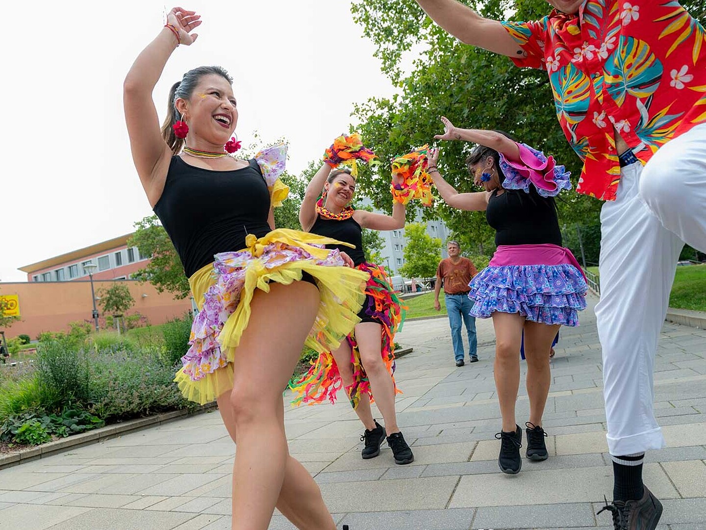 Eine Samba-Tänzerin reißt beim Karneval der Kulturen ihr Bein in die Höhe und lacht andere Tänzer und Tänzerinnen dabei an.