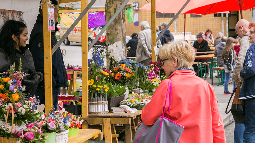 Seniorin läuft an Blumenständen vorbei.