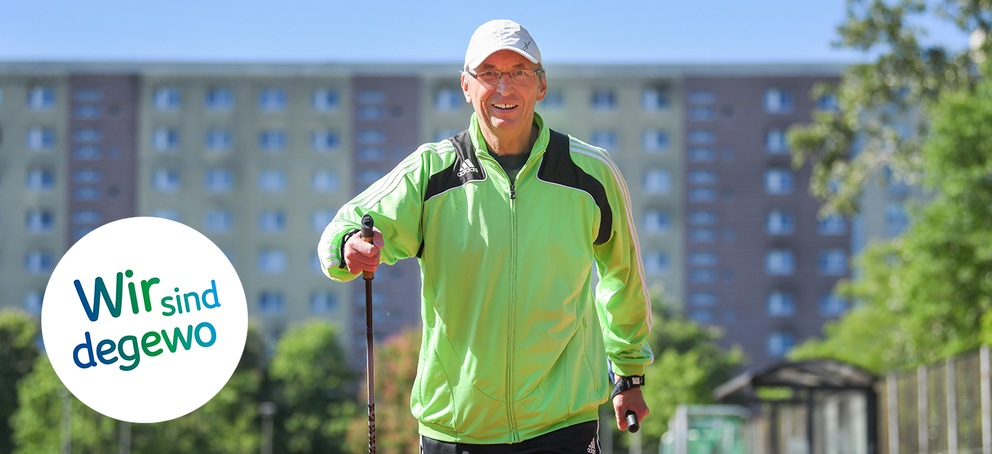 Das Bild zeigt Uwe Tolle beim Nordic Walking auf einen Sportplatz. Er trägt eine grüne Laufjacke und ein Basecap. Im Hintergrund ist verschwommen ein Plattenbau in Marzahn zu erkennen. 