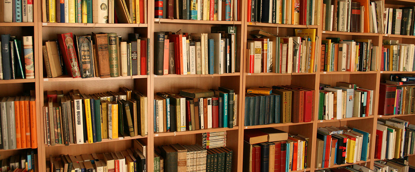Nahaufnahme eines Bücherregals aus Holz, bis oben hin gefüllt mit Büchern.