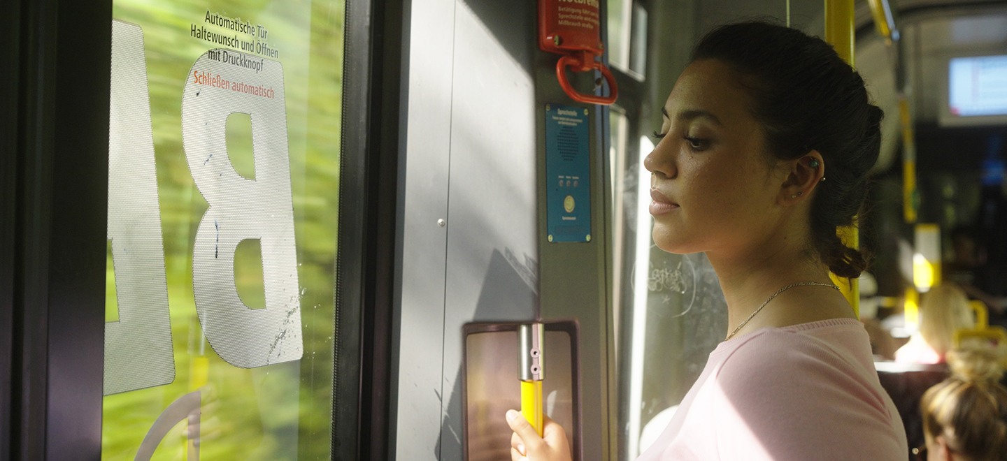 Eine junge Frau steht in der Tram und schaut aus dem Fenster.